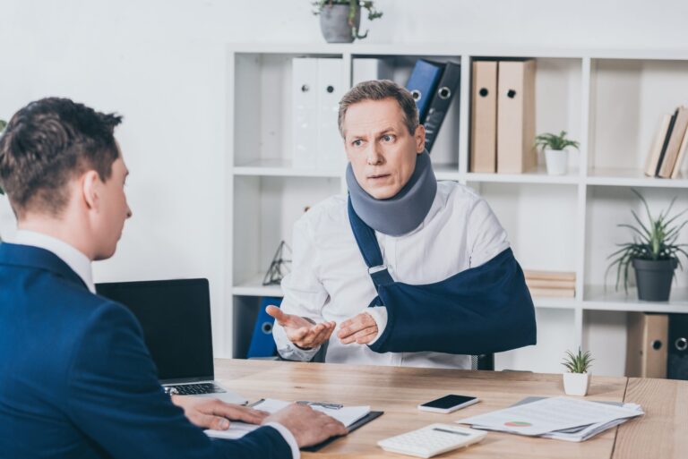 middle aged worker in neck brace with broken arm sitting at tabl