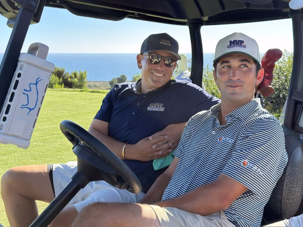 Jake Adams in an MVP Accident Attorneys cap riding in a golf cart above the Pacific.
