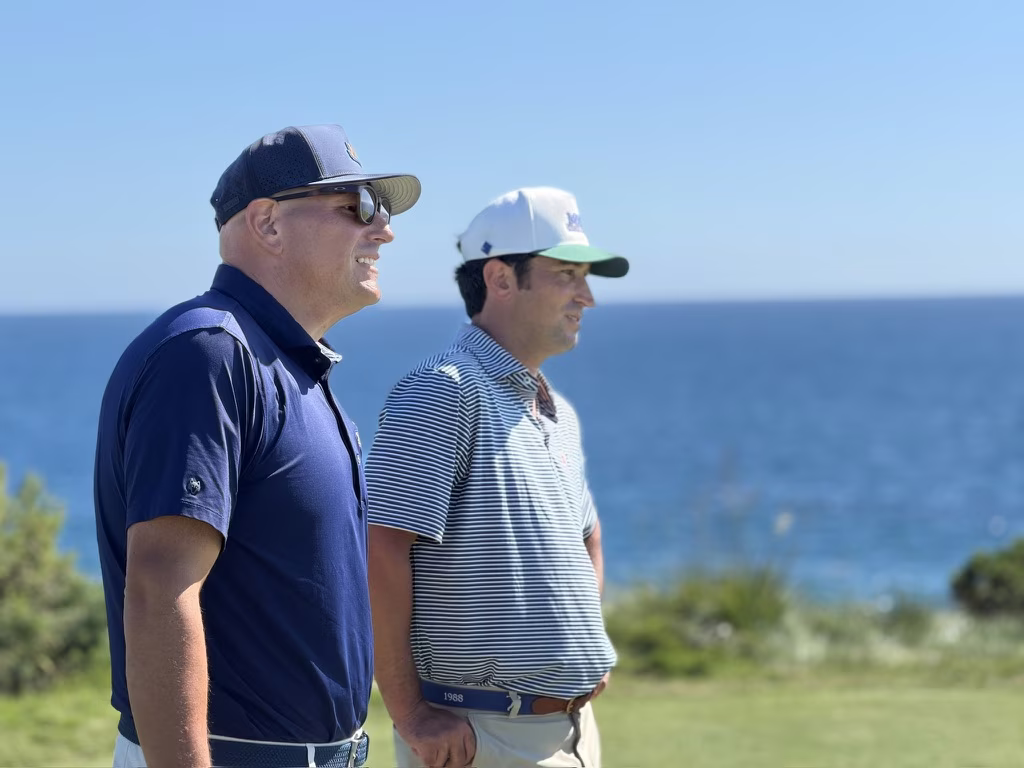 Two golfers talking on an oceanside tee box during a Jake Adams and MVP round.